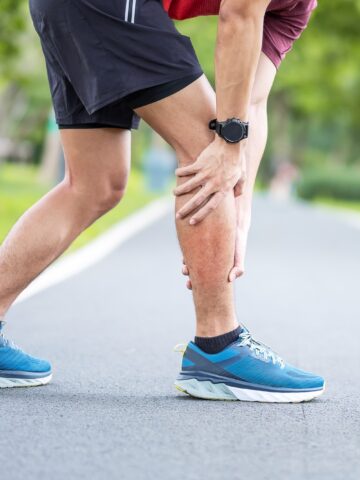 A man holding his calf on the street mid-run in pain.