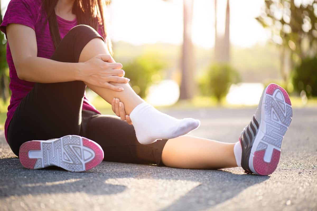 A woman sitting outside after a run holding her calf.