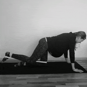 A woman doing resistance band donkey kicks for glute strength.