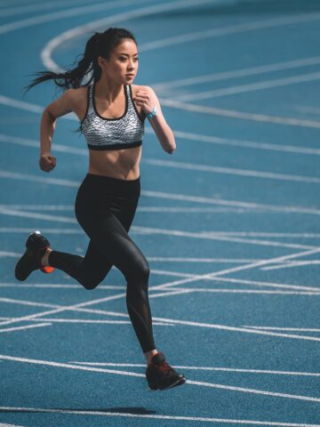 A slim woman doing mile repeats on a blue track.