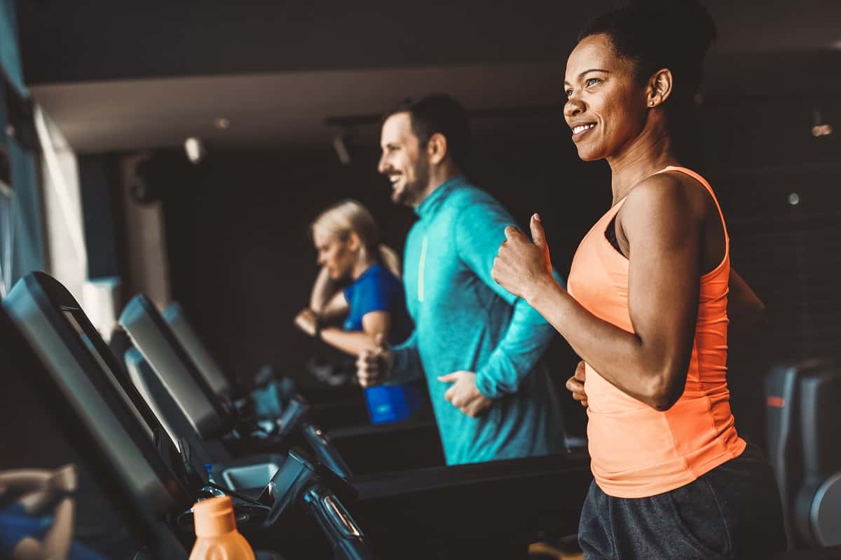 A woman in an orange shirt running on the treadmill, next to a man in a teal shirt running on the treadmill.