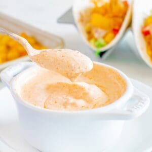 A spoon taking chipotle greek yogurt taco sauce out of a white bowl.