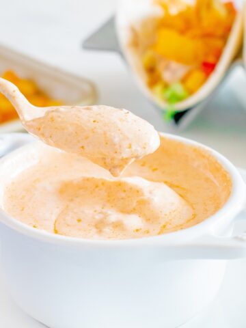 A spoon taking chipotle greek yogurt taco sauce out of a white bowl.