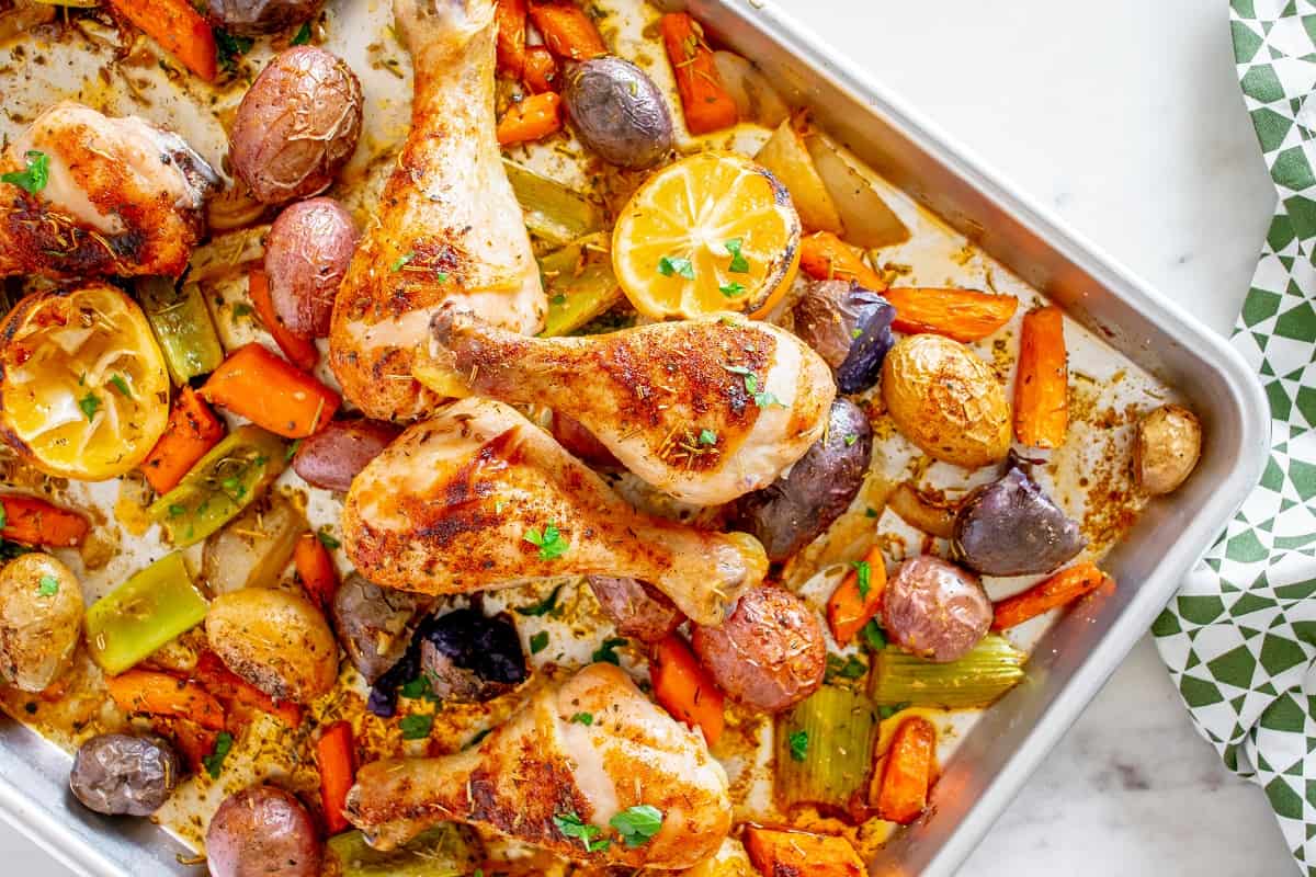 A sheet pan with just-baked chicken drumsticks and vegetables, next to a napkin.