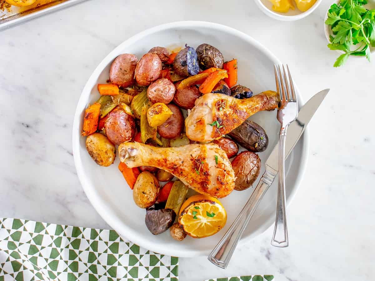 A white plate filled with veggies and chicken drumsticks.