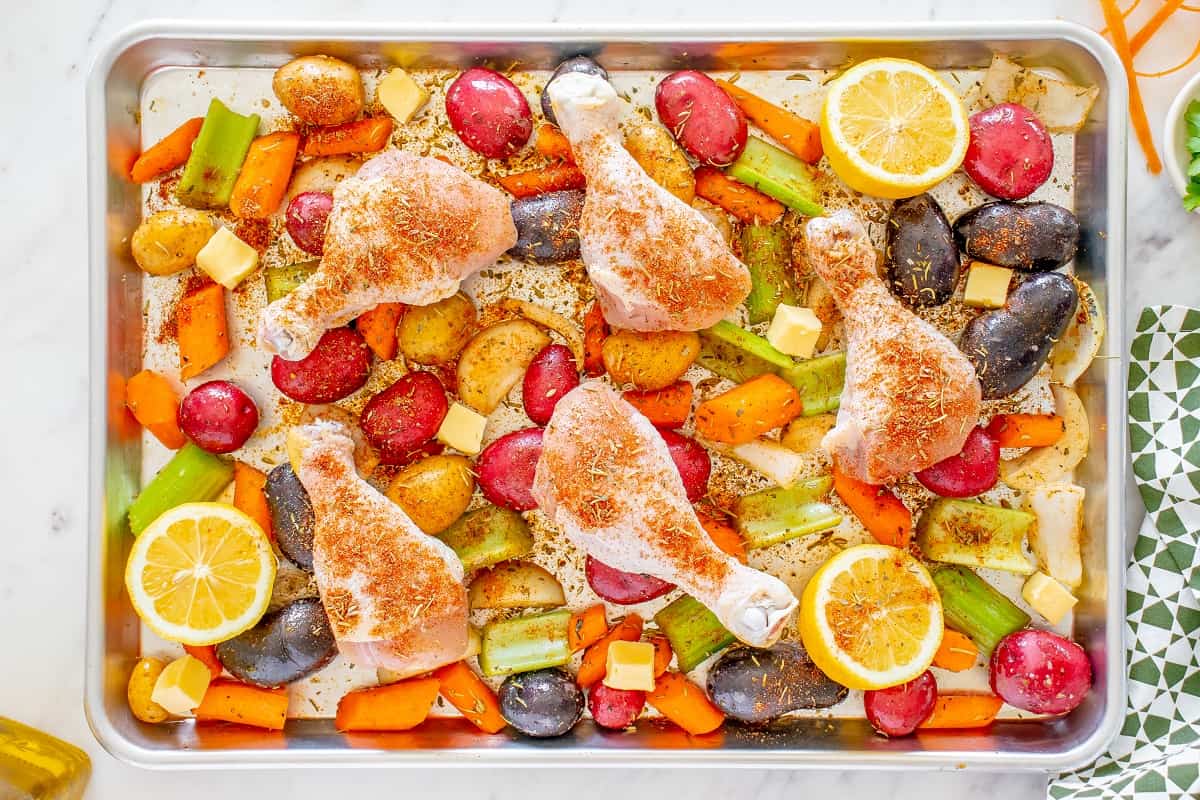 Uncooked chicken and vegetables on a sheet pan, seasoned with salt, pepper, paprika, garlic powder, and Italian seasoning.