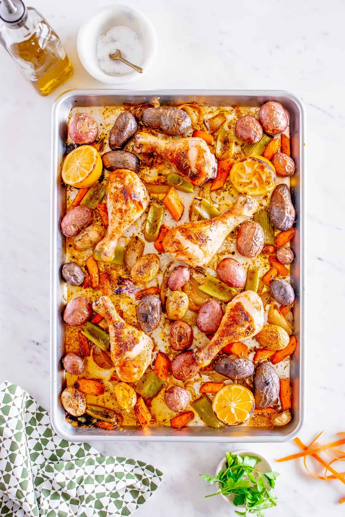 A sheet pan meal next to a napkin, bottle of olive oil, and fresh parsley.