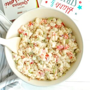 A bowl of greek yogurt macaroni salad with a wooden spoon in the side.