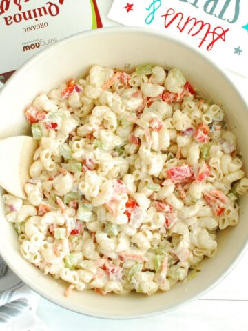 A bowl of greek yogurt macaroni salad with a wooden spoon in the side.