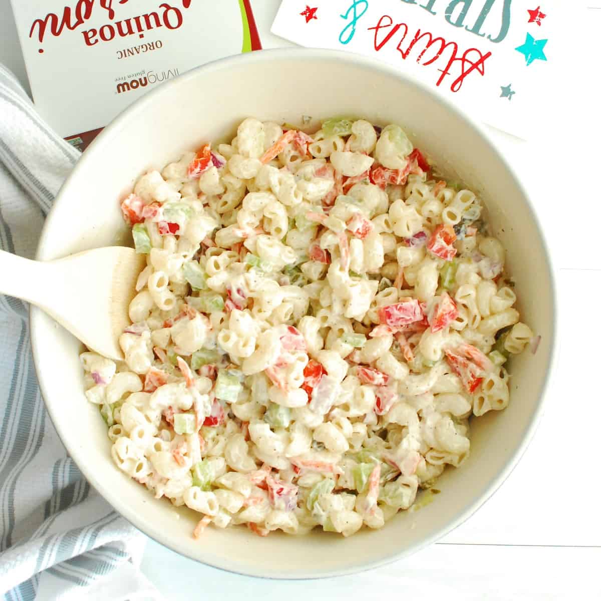 A bowl of greek yogurt macaroni salad with a wooden spoon in the side.
