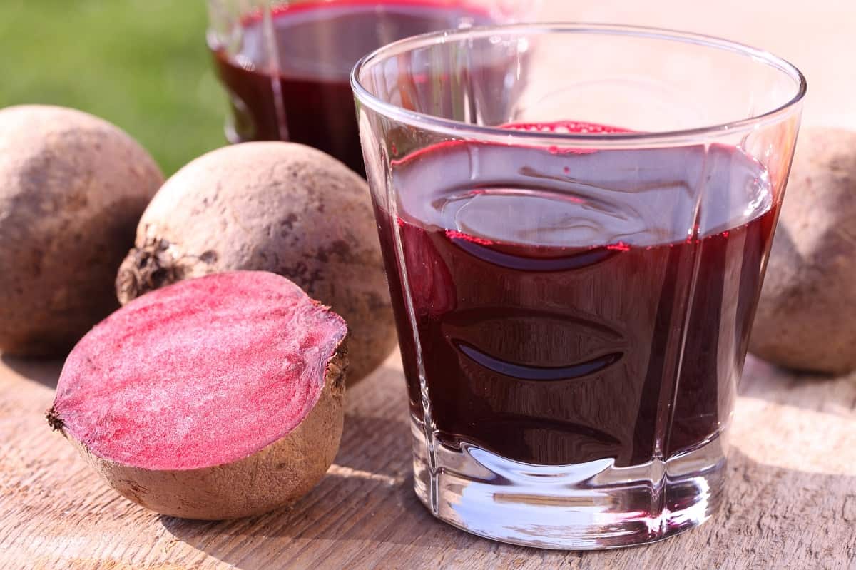 A small glass of beet juice on a table next to a beet.