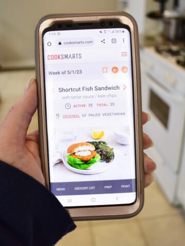A woman's hand holding a phone looking at her Cook Smarts meal plan.