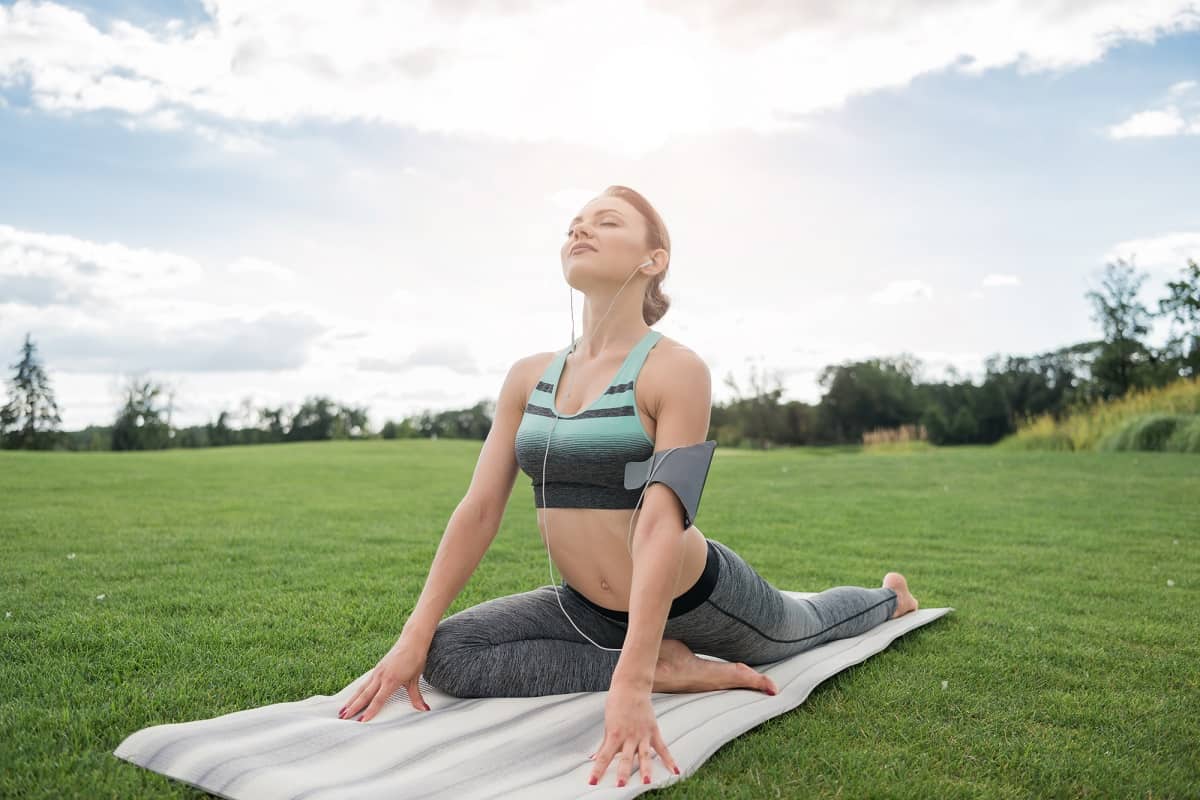 A woman doing a pigeon pose on a yoga mat outside after a run.