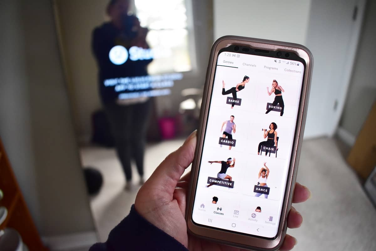 A woman's hand holding a phone displaying the different types of classes on the lululemon studio app.