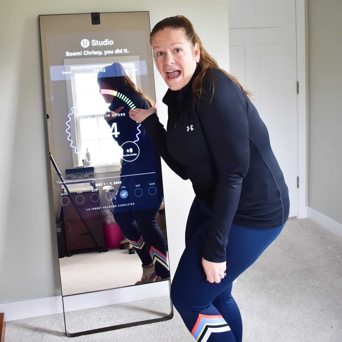 A woman standing next to her lululemon studio mirror after finishing a class.