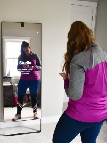 A woman selecting a class on her phone in front of the lululemon studio mirror.