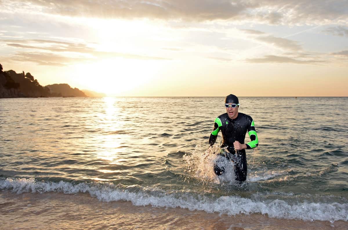 A triathlete running out of ocean water in a wetsuit.