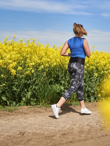 A woman running on a dirt path past a field of flowers while training for a marathon.