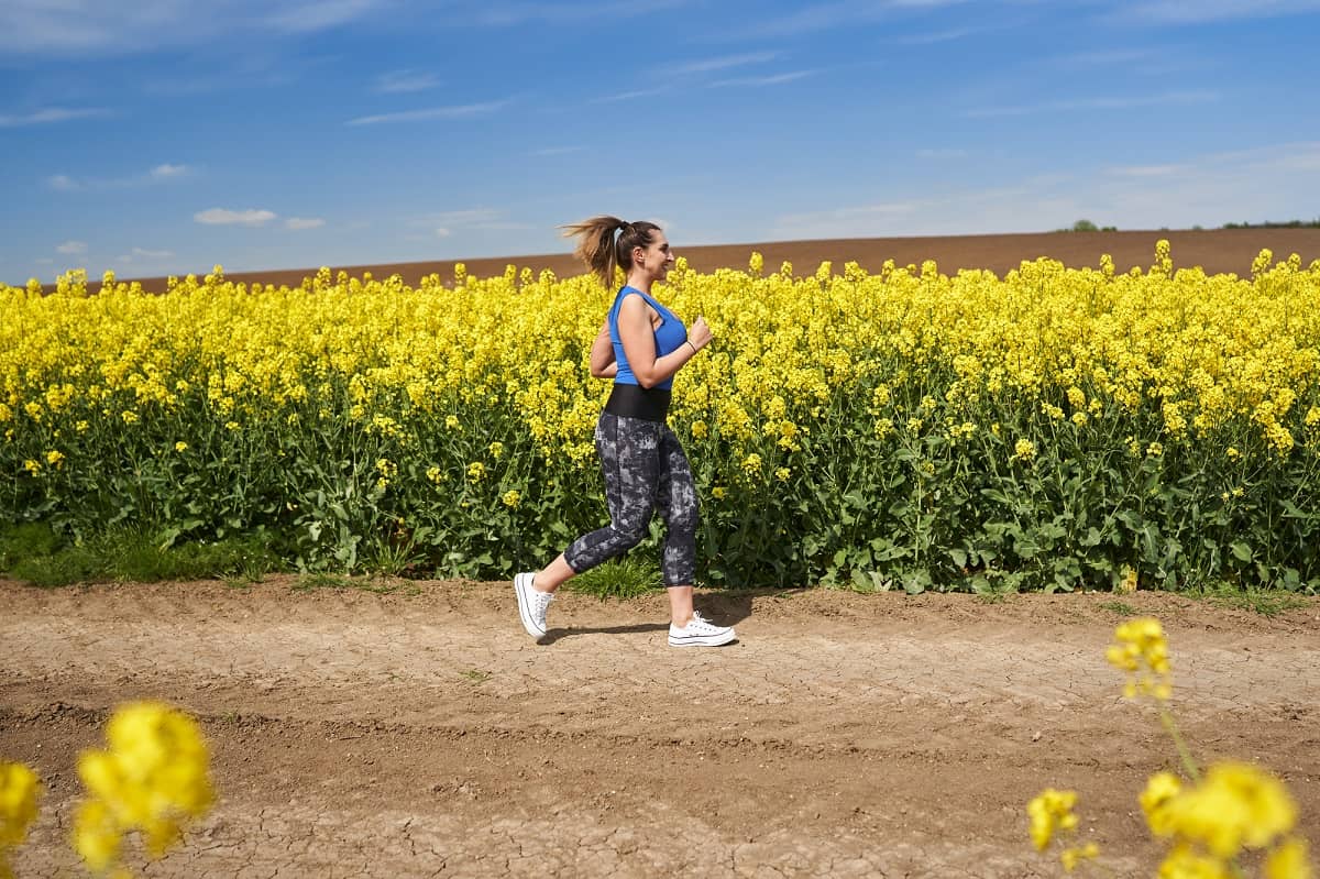 A woman running by a field of flowers outside while training for her marathon.