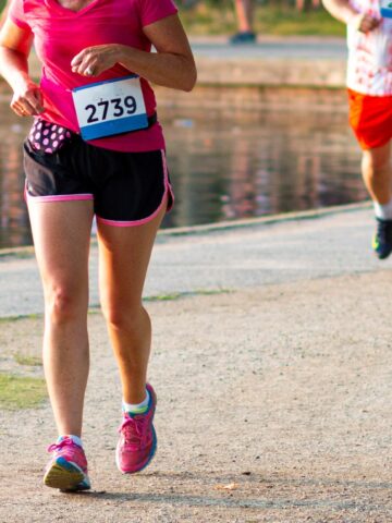 A woman running a 5K race in a pink t shirt and shorts.