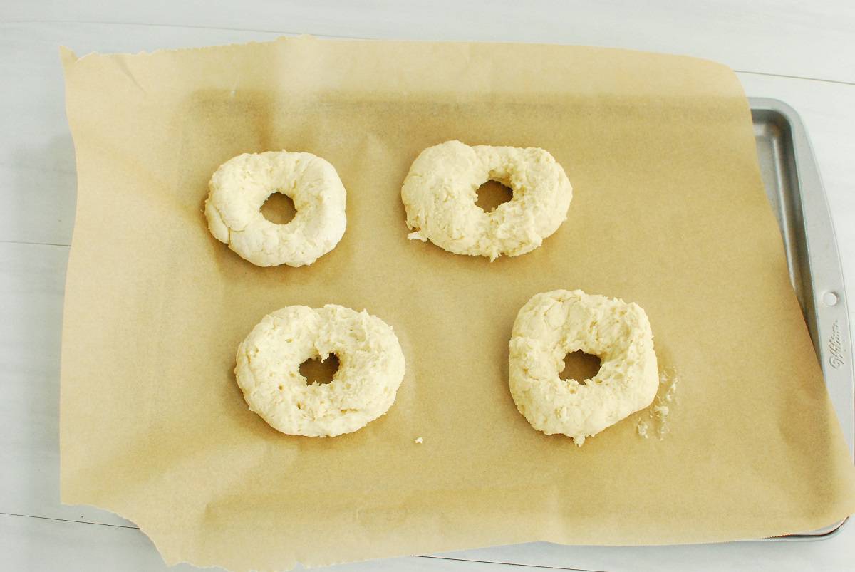 Four pieces of bagel dough on a baking sheet.