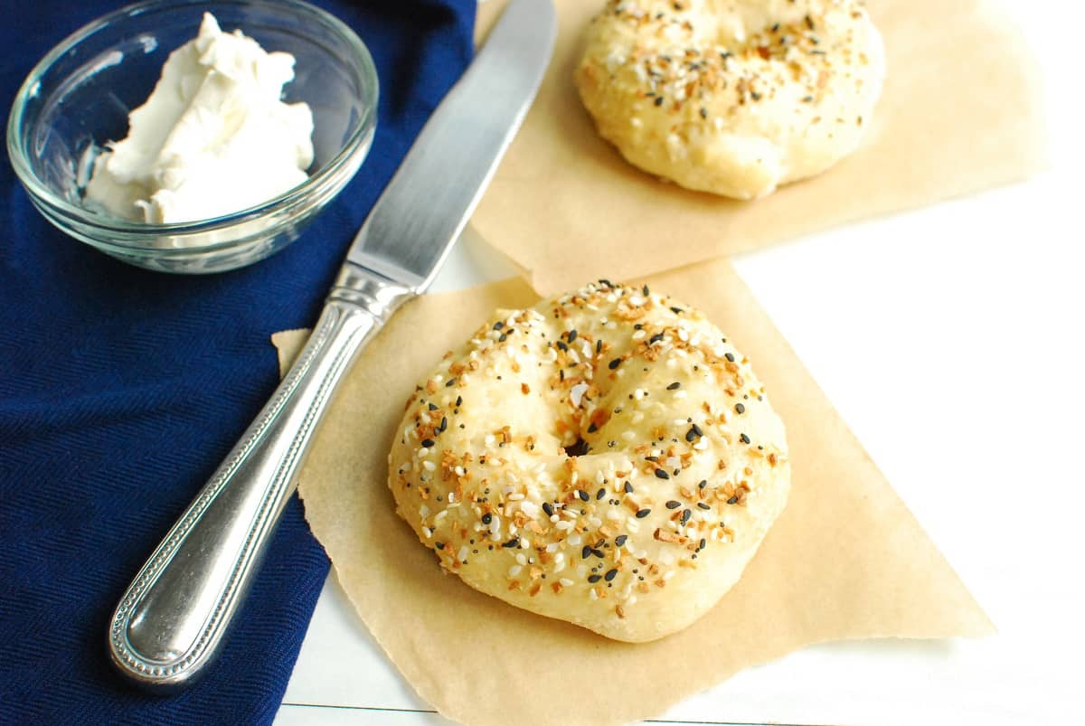 Two cottage cheese bagels next to a blue napkin, knife, and cream cheese.