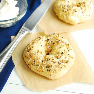 A cottage cheese bagel on parchment paper next to a napkin, knife, and cream cheese.