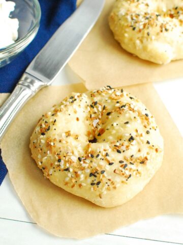 A cottage cheese bagel on parchment paper next to a napkin, knife, and cream cheese.