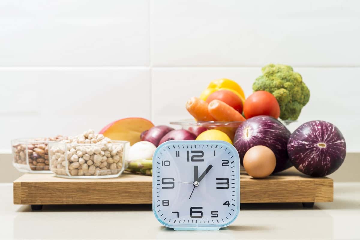 Fruits, vegetables, and nuts on a cutting board, with a clock in front of it illustrating an intermittent fasting concept.