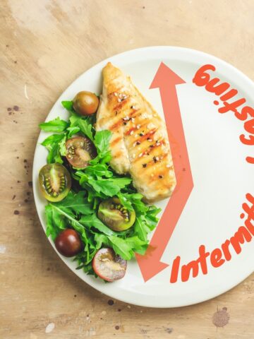 A plate illustrating an intermittent fasting concept, with part of the plate containing food, next to a knife and fork.