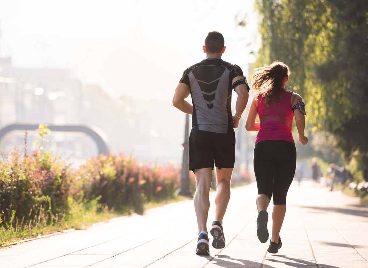 A young couple running together along a paved path.