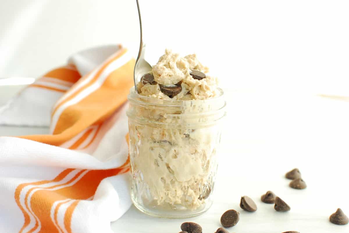 A small jar filled with cottage cheese cookie dough, next to a napkin and some chocolate chips.