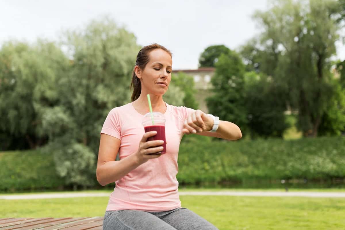 A runner sitting in the park drinking a smoothie.