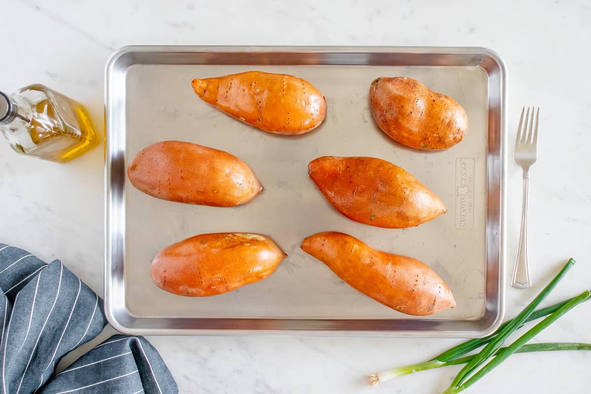 Sweet potatoes rubbed with oil on a baking sheet.