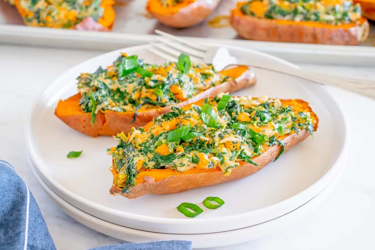 Two savory twice baked sweet potatoes on a white plate, garnished with green onions.
