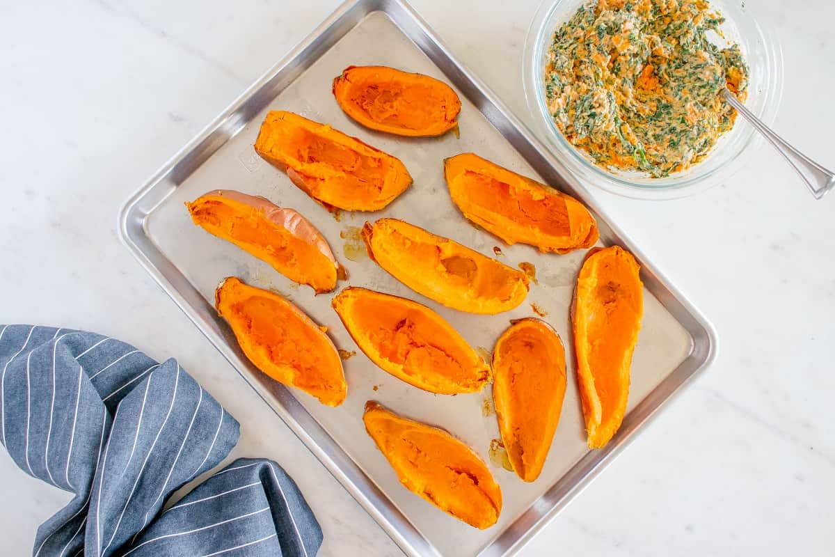 Sweet potatoes on a baking sheet after some of the flesh has been removed.