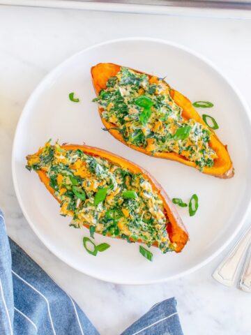 Two savory twice baked sweet potatoes on a white plate next to a blue napkin.