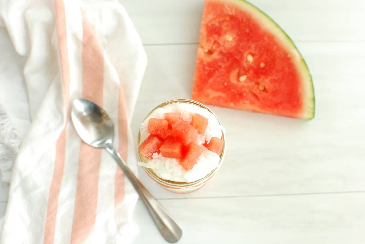 An overhead shot of a watermelon parfait next to a spoon, napkin, and slice of watermelon.