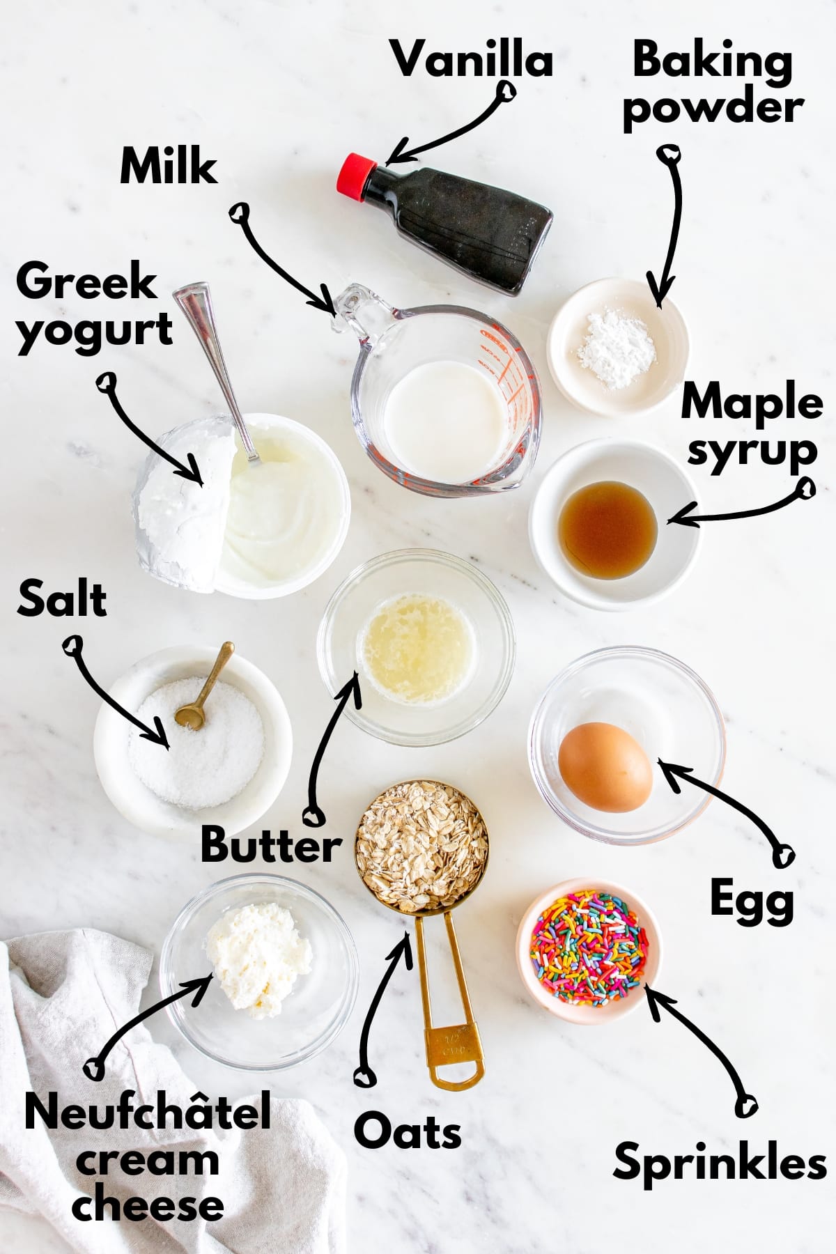 All of the ingredients to make baked oats on a white table next to a napkin.