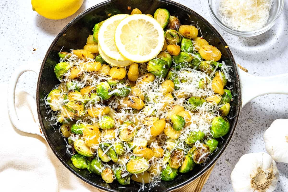 A skillet full of brussels sprouts and gnocchi topped with parmesan.