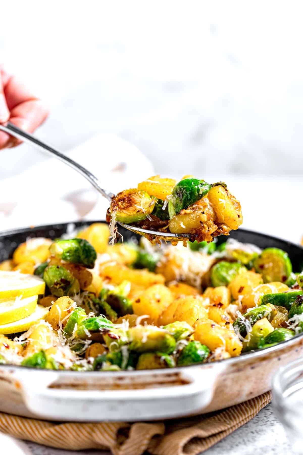 A woman using a large spoon to scoop up some skillet gnocchi and brussels sprouts.