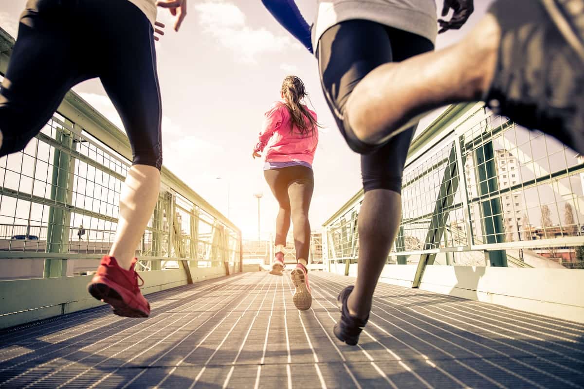 A group of runners running outside over a bridge.