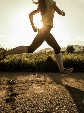 A runner sprinting on a dirt road with some fields and the sun in the background.