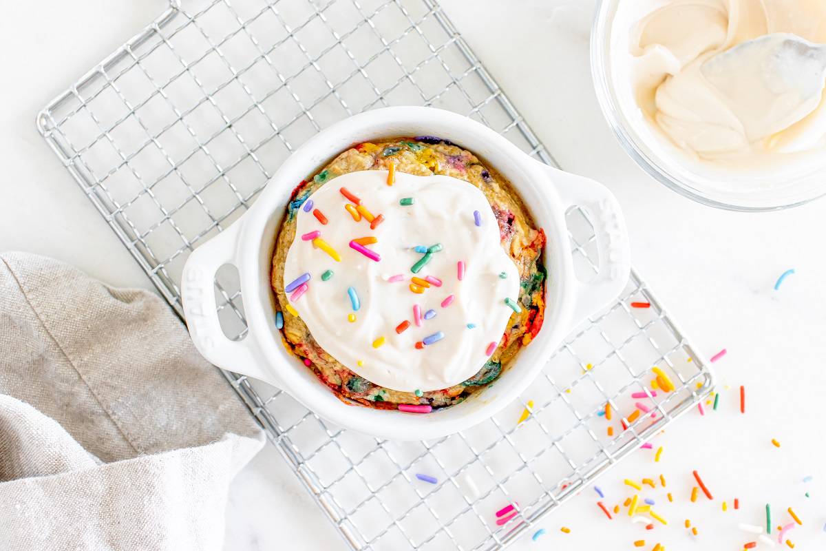 Birthday cake oatmeal in a ceramic dish with frosting on top, sitting on a cooling rack.