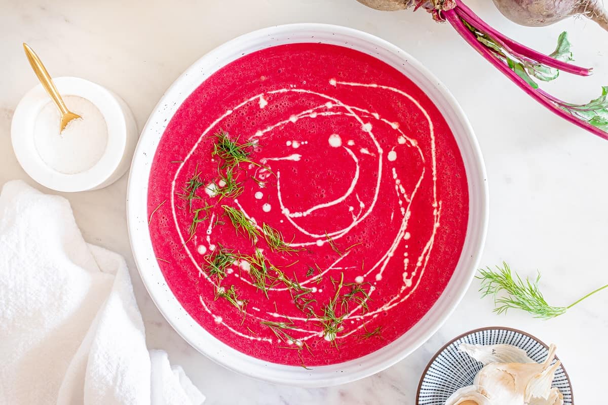 A bowl of beet soup garnished with half and half and dill.