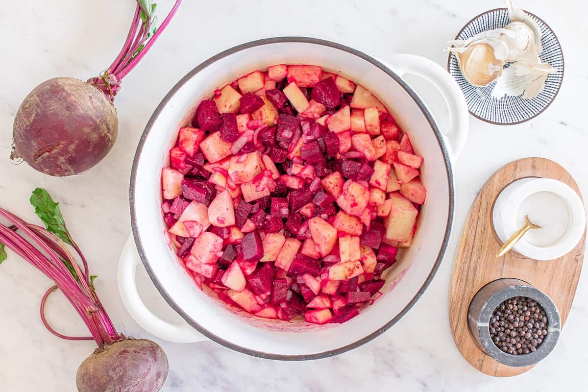 A pot with beets, onion, apple, potato, garlic, salt and pepper in it.