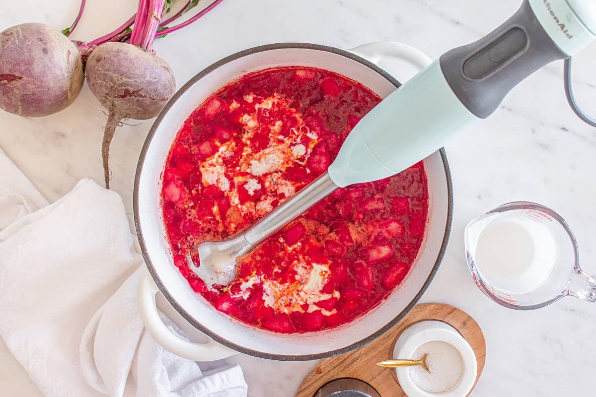 A pot of beet soup with half and half added, about to be blended by an immersion blender.