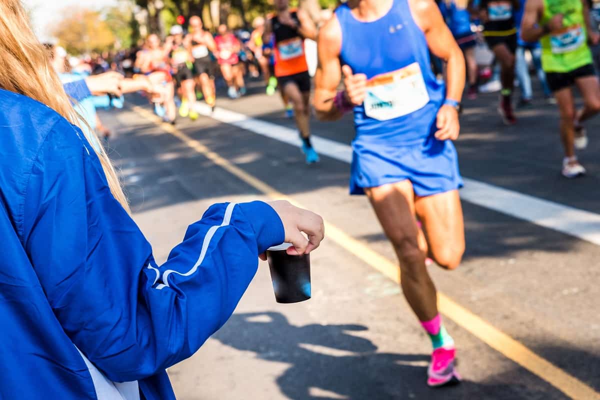 A race volunteer holding out an electrolyte drink in a cup for runners during a road race.