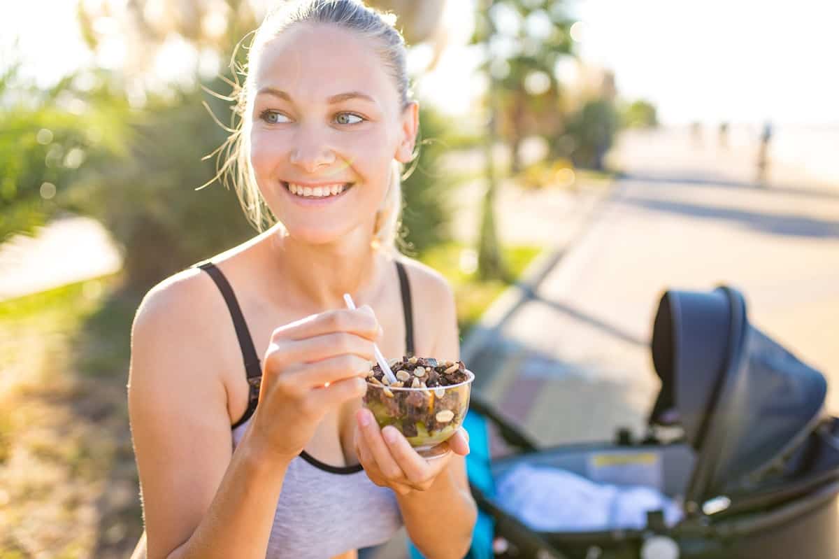 A female runner eating a smoothie bowl outside.