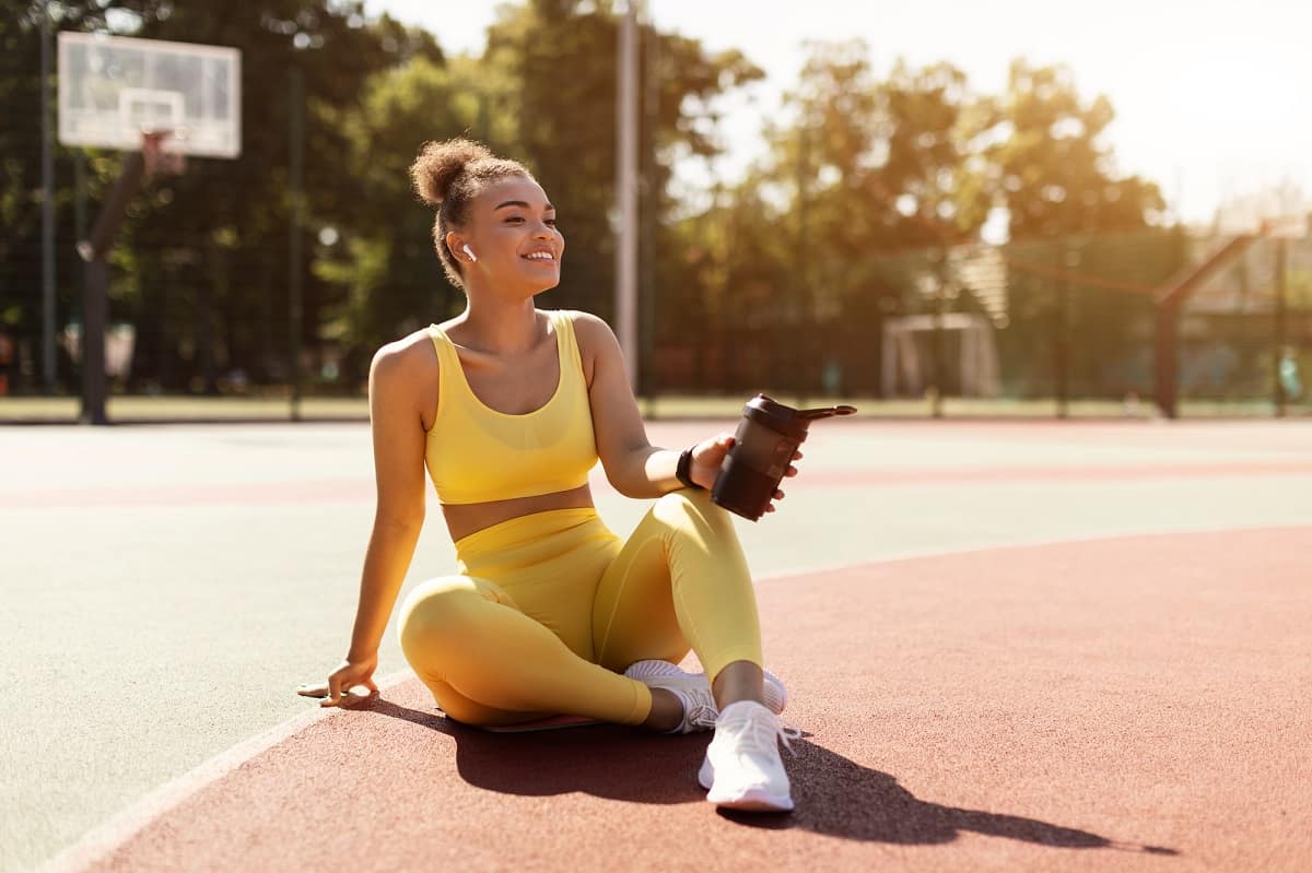 A female runner sitting on a track with a protein shake in her hand.